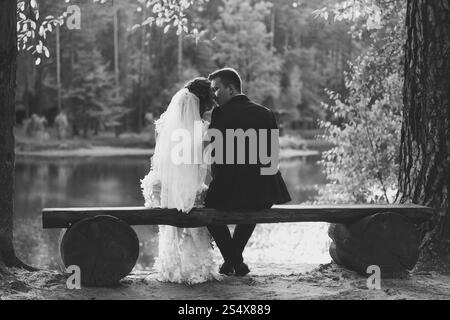 Photo en noir et blanc de mariée et mariée s'embrassant sur le banc à Riverbank Banque D'Images