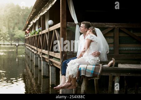Belle mariée et marié assis sur la jetée et regardant la rivière et la forêt Banque D'Images