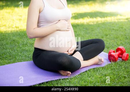 Photo gros plan de l'enceinte active woman sitting on grass at park et toucher gros ventre Banque D'Images