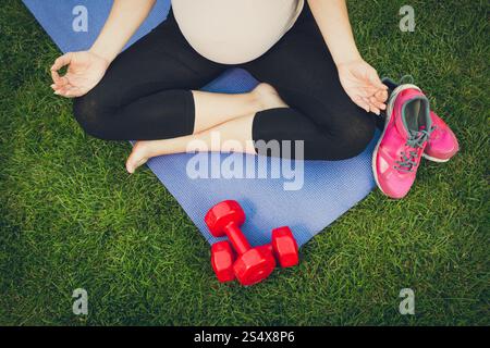 Vue rapprochée de la femme enceinte en méditant sur le tapis de fitness at park Banque D'Images
