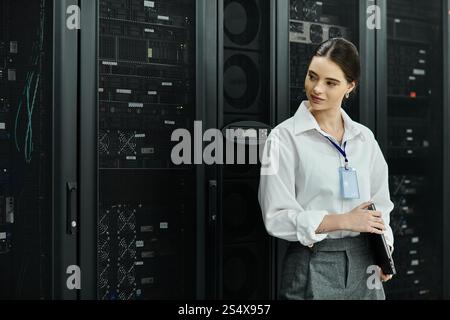 Une femme professionnelle en chemise blanche surveille les systèmes de serveur dans une installation technologique moderne. Banque D'Images