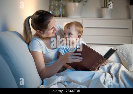 Portrait de jeune femme au lit avec son bébé dans la nuit et la tenue de grand livre Banque D'Images