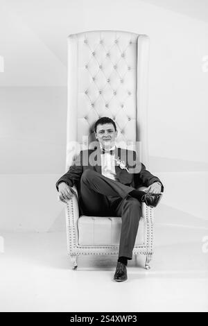 Le noir et blanc portrait of handsome man posing élégant au studio en fauteuil Banque D'Images
