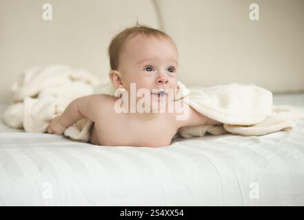 Portrait drôle de surprise baby boy lying under blanket on bed Banque D'Images