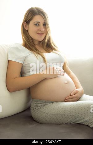 Belle femme enceinte se relaxant sur le canapé et tenant les mains sur le ventre Banque D'Images