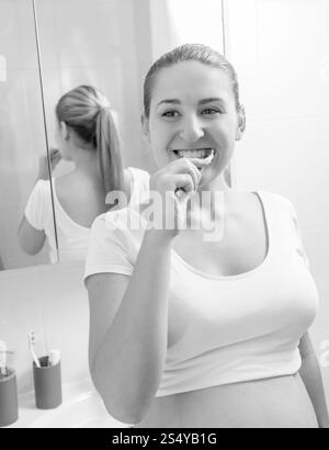 Portrait monochrome d'une jeune femme enceinte se brossant les dents à la salle de bain Banque D'Images