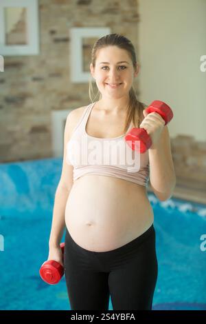 Portrait d'une femme enceinte souriante soulevant des haltères Banque D'Images