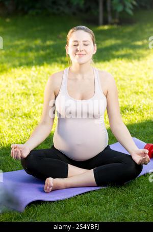Femme enceinte relaxant et méditant au parc Banque D'Images