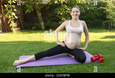 Jeune femme enceinte souriante s'étirant au parc à la journée ensoleillée Banque D'Images