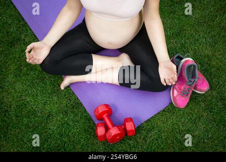 Gros plan d'une femme enceinte méditant sur un tapis de fitness à l'extérieur Banque D'Images