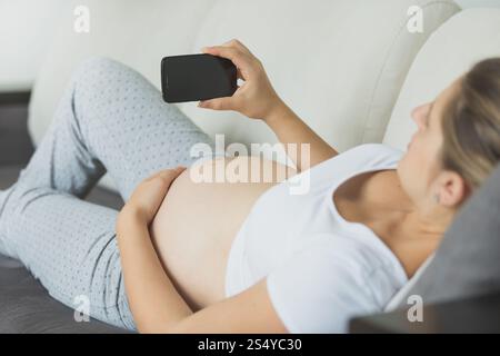 Gros plan d'une femme enceinte se relaxant sur un canapé et utilisant un téléphone portable Banque D'Images