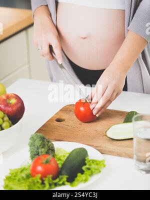 Gros plan d'une femme enceinte coupant des tomates fraîches pour la salade Banque D'Images