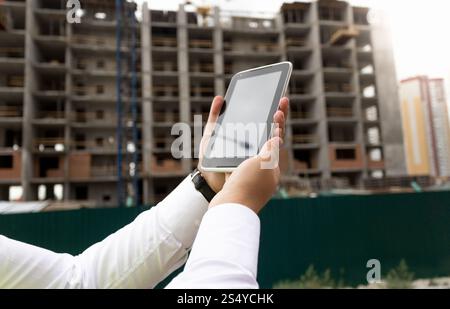 Gros plan de jeune main masculine tenant la tablette numérique avec le site de construction sur fond Banque D'Images