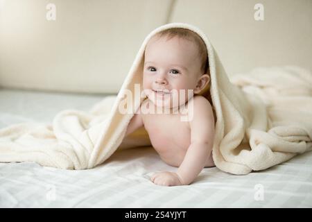 Portrait de bébé garçon surpris couché sous une couverture sur le lit Banque D'Images