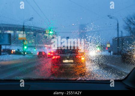Conduite dans les chutes de neige de nuit à Moscou - arrière-plan flou avec vue bien que les gouttes de neige fondante sur le pare-brise dans la soirée d'hiver Banque D'Images