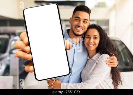 Famille musulmane aimant montrant un smartphone avec écran vierge, achetant la voiture Banque D'Images