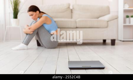 Femme frustrée assise près des balances de poids à la maison, Panorama Banque D'Images