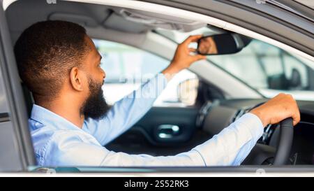 Jeune homme noir assis à l'intérieur de la voiture et ajustant le rétroviseur Banque D'Images