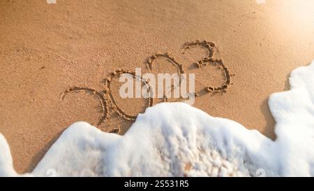 Gros plan des vagues océaniques roulant plus de 2023 numéros écrits sur du sable humide. Concept de nouvel an, Noël et voyage sur les vacances d'hiver. Gros plan Banque D'Images