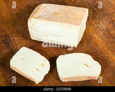 Fromage Taleggio italien local tranché à partir de lait complet de vaches sur une planche à découper en bois foncé Banque D'Images