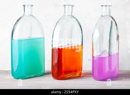 trois bouteilles avec des solutions d'aquarelle de couleur sur panneau de bois gris près du mur de béton gris. trois bouteilles avec des solutions d'aquarelle sur gris Banque D'Images