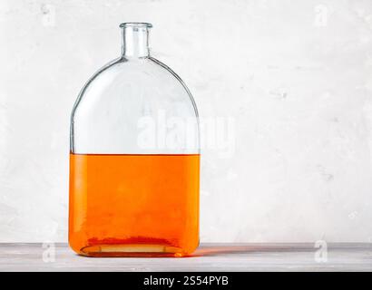 flacon en verre avec solution d'aquarelle orange sur panneau de bois gris près du mur de béton gris. flacon avec solution d'aquarelle orange sur gris Banque D'Images