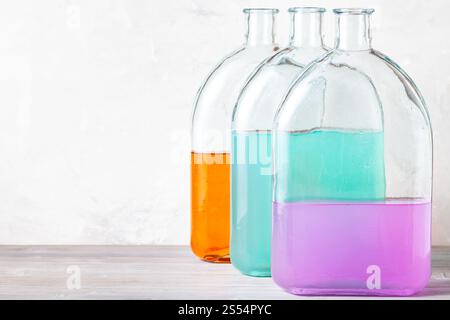 bouteilles en verre avec des solutions d'aquarelle de couleur sur panneau de bois gris près du mur de béton gris. bouteilles en verre avec des solutions d'aquarelle sur gris Banque D'Images