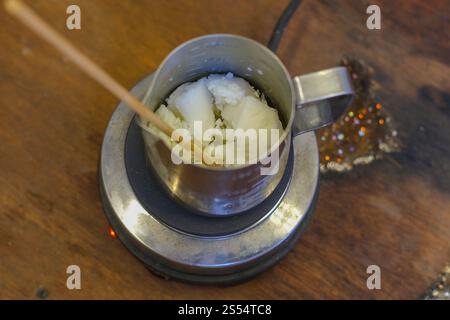 Gros plan d'un bol en fer sur un poêle où la cire d'abeille est fondue pour faire des bougies. Banque D'Images