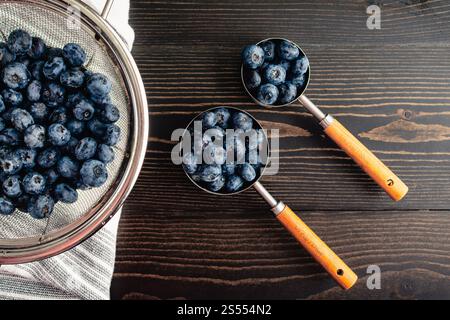 Bleuets dans des tasses à mesurer sur une table en bois : les bleuets frais dans des tasses à mesurer nichent à une passoire de bélubrries lavées avec des gouttes d'eau Banque D'Images