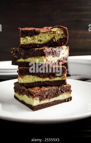 Cheesecake Matcha empilés Brownies vue de côté : profil des brownies au chocolat noir avec remplissage de fromage à la crème de thé vert empilés sur une assiette à dessert blanc Banque D'Images
