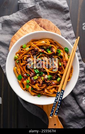 Nouilles à l'huile de Chili à l'échalote servies dans un bol Ramen : nouilles lo mein chaudes et épicées garnies de piment croustillant et d'échalotes servies avec des baguettes Banque D'Images