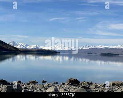 Lac serein reflétant des sommets montagneux enneigés sous un ciel bleu clair en Nouvelle-Zélande Banque D'Images