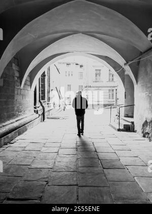 Photo noir et blanc de silhouette masculine marchant sur la vieille rue étroite sous une grande arche. Image en noir et blanc de la silhouette masculine marchant sur le vieux étroit Banque D'Images