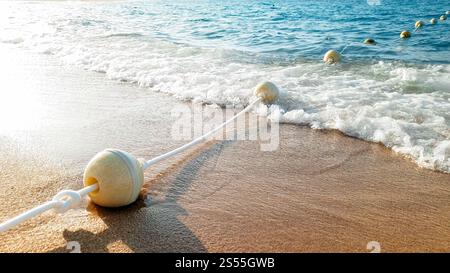 Gros plan belle photo de longue ligne de bouées flottantes reliées par une corde flottant dans la mer et allongée sur une plage de sable Banque D'Images