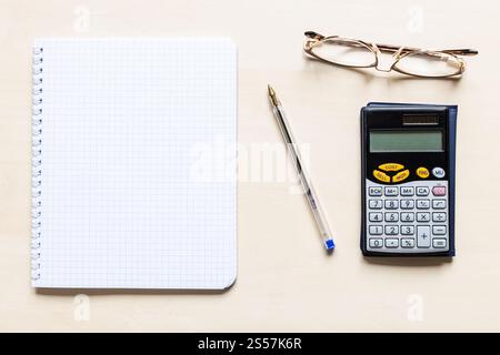 vue de dessus d'une feuille vierge de papier quadrillé, d'un stylo, de lunettes et d'une calculatrice financière sur un panneau en bois brun clair Banque D'Images