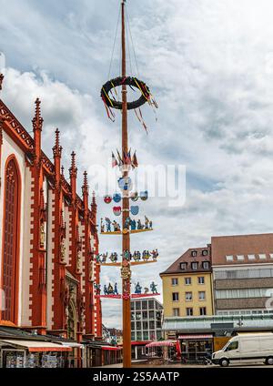 Un Maypole décoratif orné de divers emblèmes et ornements, situé à proximité de bâtiments historiques sur une place du marché européen. Capturé par temps nuageux Banque D'Images
