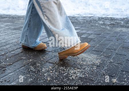 Produits chimiques antigivrage. Homme marchant dans la rue traité avec du sel technique ou des produits chimiques de dégivrage Banque D'Images