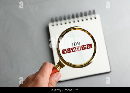 Concept de recherche d'emploi. Femme regardant les mots dans le carnet à travers une loupe sur la table grise, gros plan Banque D'Images