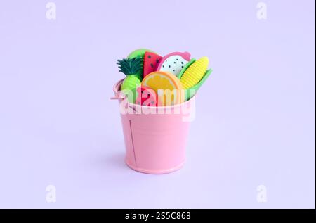Divers fruits frais dans un petit seau rose sur fond violet. Récolte saisonnière des fruits. Travail pour les agriculteurs. Divers fruits frais dans un petit seau rose sur Banque D'Images