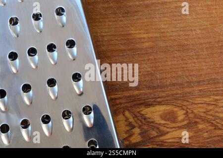 La râpe chromée repose sur la planche à découper avec beaucoup de cicatrices de la hache et du couteau. Image d'arrière-plan pour les recettes de cuisine Banque D'Images