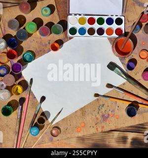 Image de fond montrant l'intérêt pour la peinture à l'aquarelle et choisi Une feuille de papier vierge, entourée de pinceaux, de boîtes de conserve avec de la peinture à l'aquarelle et Banque D'Images