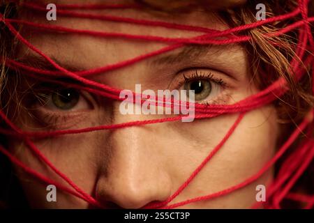 Gros plan d'une partie du visage féminin avec de légères rides et de grands yeux verts, sa tête recouverte de fils rouges Banque D'Images