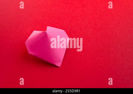 Origami coeur en papier rose isolé sur un fond rouge vierge. Carte de Saint-Valentin. Origami coeur en papier rose isolé sur un fond rouge Banque D'Images