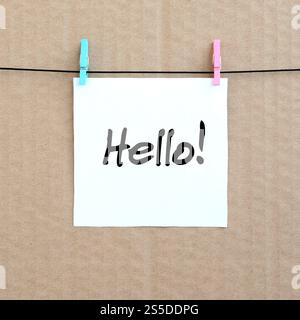 Bonjour ! Note est écrit sur un autocollant blanc qui est suspendu avec une pince à linge sur une corde sur un fond de carton brun Banque D'Images