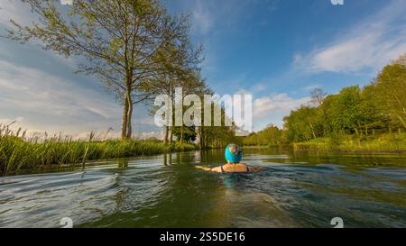 Vue arrière d'une femme portant un bandeau tricoté turquoise nageant sauvage dans le lac Monet à Pool Bridge Farm. York Banque D'Images