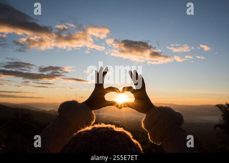 Silhouette des mains formant un coeur avec le lever du soleil Banque D'Images