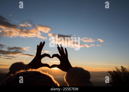 Silhouette des mains formant un coeur avec le lever du soleil Banque D'Images
