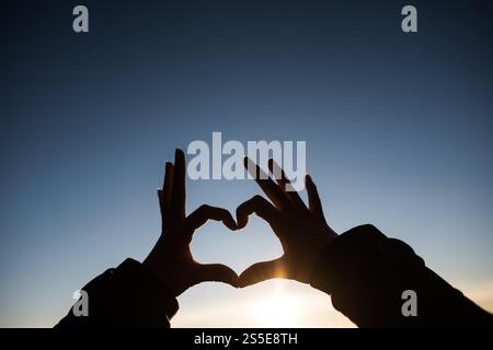 Silhouette des mains formant un coeur avec le lever du soleil Banque D'Images