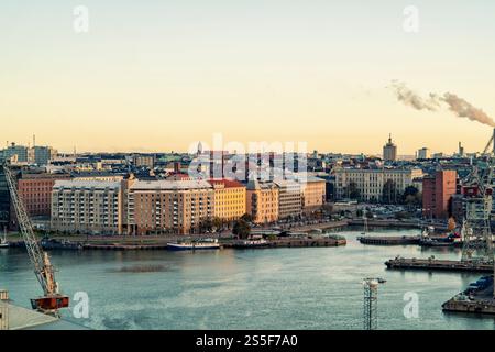 Vue aérienne d'une ville au crépuscule avec des bâtiments le long de la rivière et une zone industrielle avec des cheminées, Helsinki, Finlande Banque D'Images