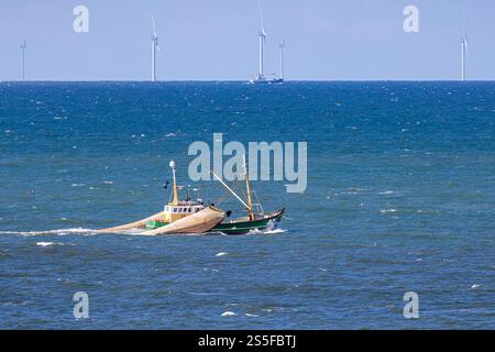 Un bateau de pêche avec des filets traînants levés devant un parc éolien en mer du Nord près d'Egmond aan Zee Banque D'Images